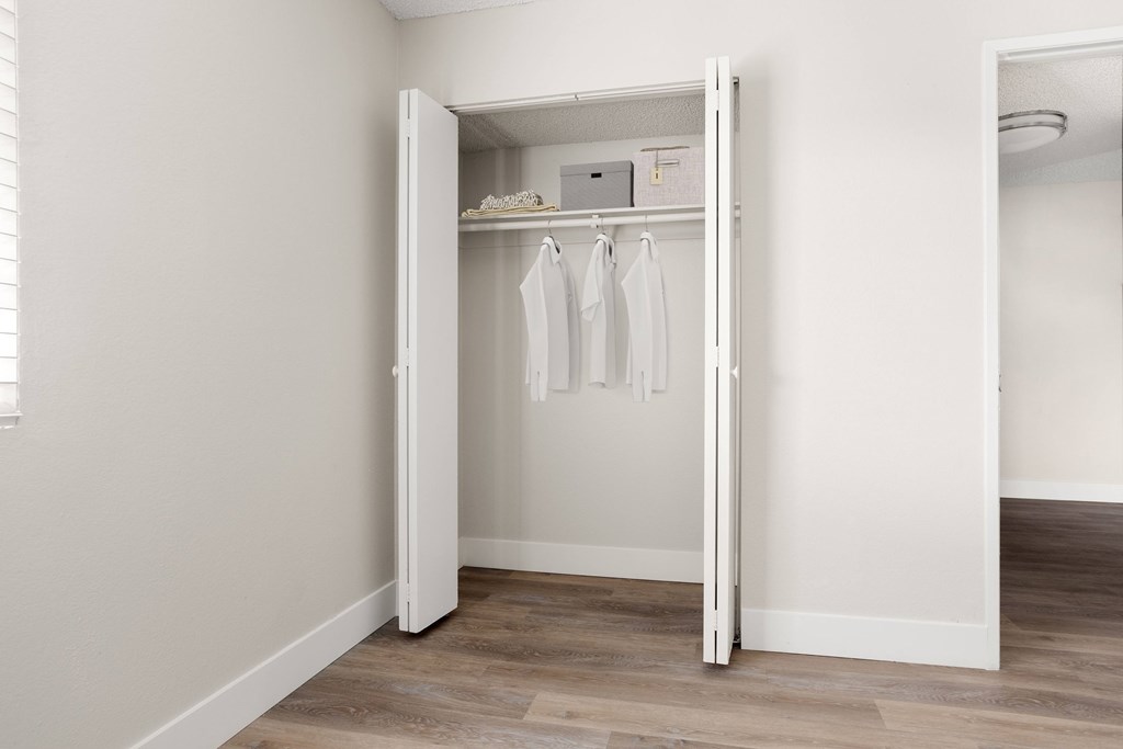 a walk in closet in a bedroom with white walls and a wooden floor